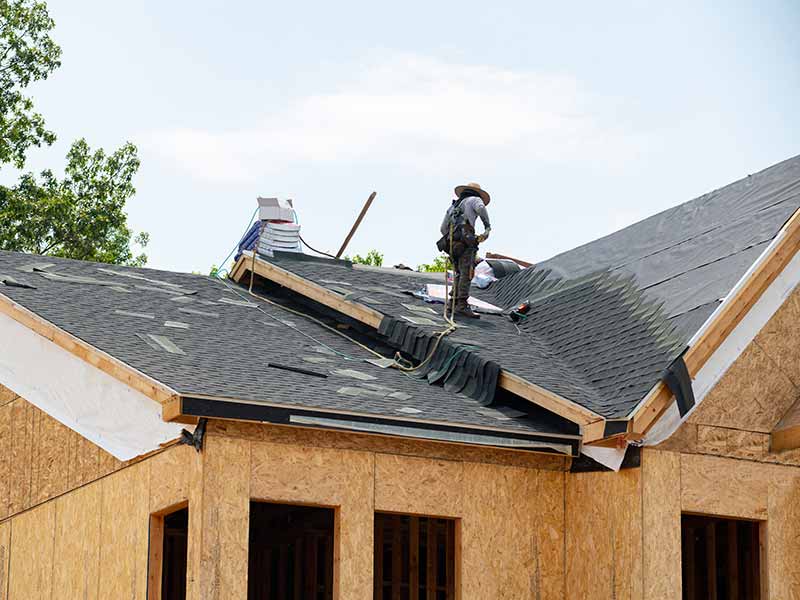 Worker installing new gray shingles on a newly constructed home
