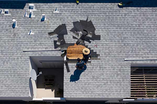 Top view of a condo with gray shingles on its roof, and the roof is getting repaired by two workers