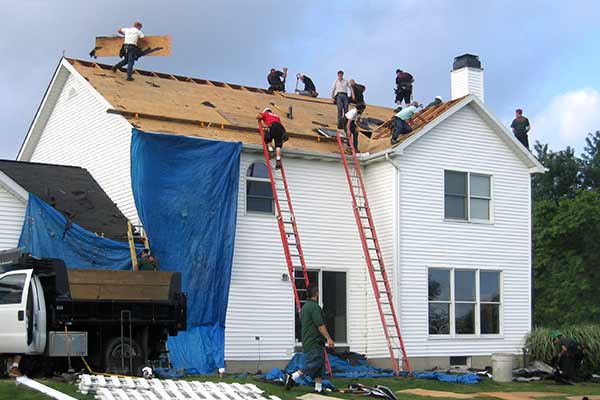 Workers on a large, two-story home replacing the wooden sheathing and shingles on the roof